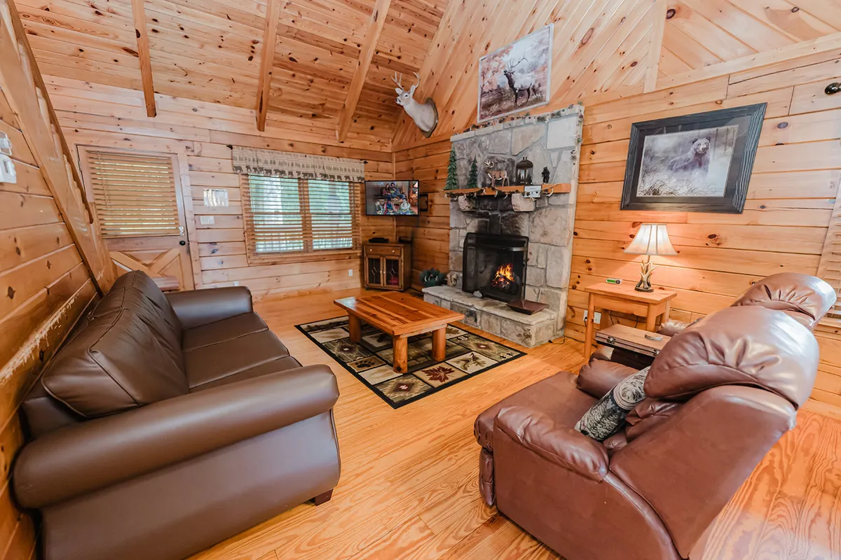 A cozy living area featuring a prominent stone fireplace, a flat-screen TV, soft sofas arranged for conversation, a coffee table ideal for games or snacks, and tasteful wall art. The lighting is warm, enhancing the inviting and communal feel of the space.