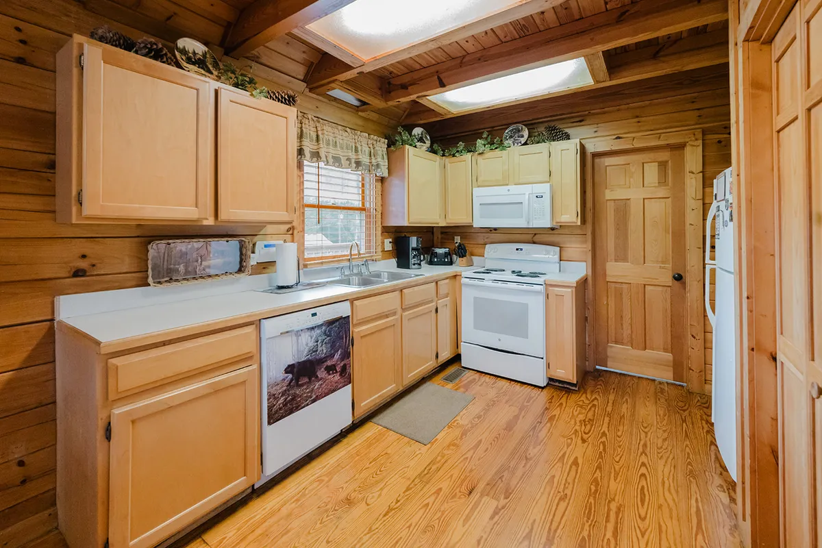 A view of the cabin's fully equipped kitchen, featuring wooden cabinets, a stove, sink, and a window that brings in natural light. The space looks welcoming and functional, ideal for preparing meals and snacks at home.