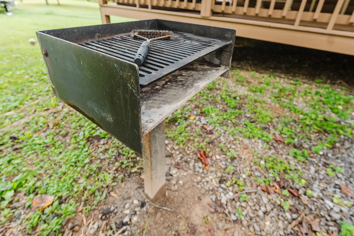A standalone charcoal grill positioned next to a gravel path and surrounded by grass, ready for outdoor barbecuing. The setting suggests ample room for gathering, cooking, and enjoying meals outside.