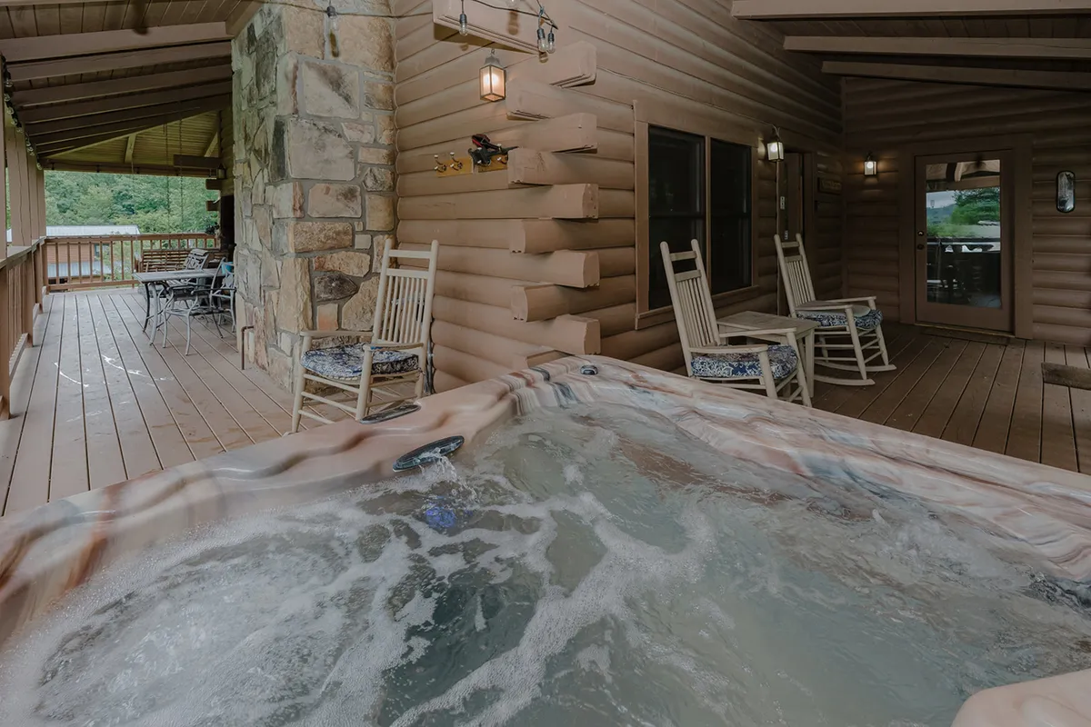 A tranquil deck space with a hot tub, two inviting rocking chairs, and a sturdy wooden railing overlooking the surrounding greenery. The setting is designed for both relaxation and socializing in nature.
