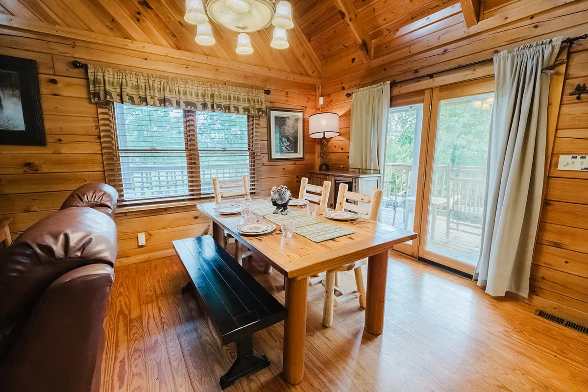 A large wooden dining table surrounded by comfortable seating, illuminated by abundant natural light streaming through oversized windows. The open layout is ideal for group meals, celebrations, or game nights, echoing the spirit of shared experiences and laughter.