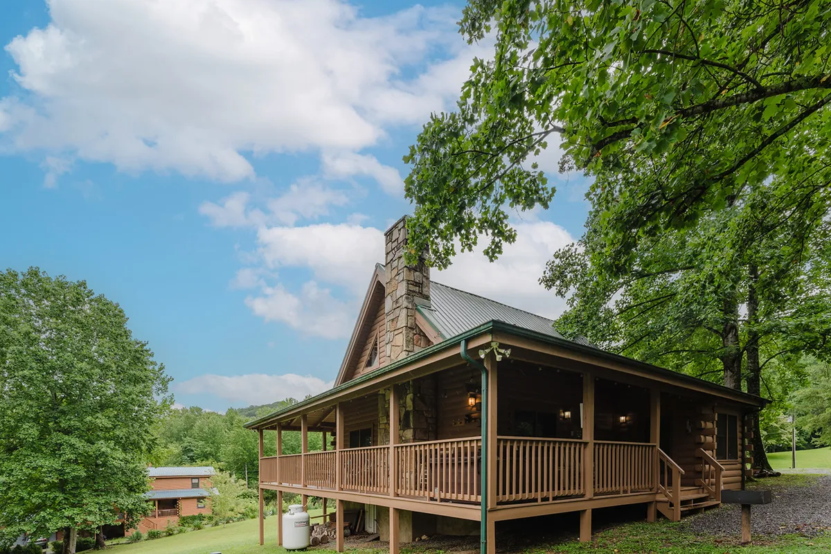 This image presents a charming log cabin, complete with a stone chimney and a spacious front porch. The porch offers plenty of room for outdoor games, family gatherings, and stargazing, providing a seamless connection between indoor comfort and outdoor exploration.