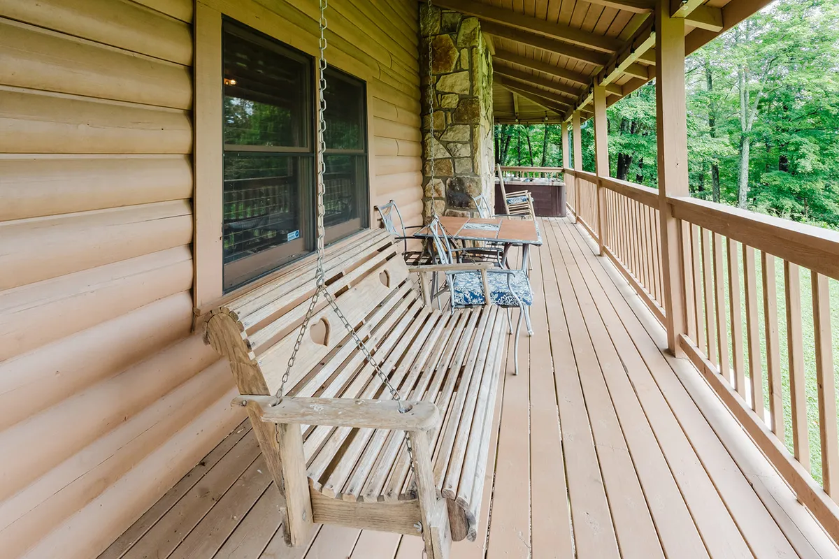 A wooden deck highlighted by a classic porch swing and a stone wall, with cozy outdoor seating and lush greenery all around. The area exudes a relaxed and inviting vibe, perfect for morning coffee or an afternoon read.
