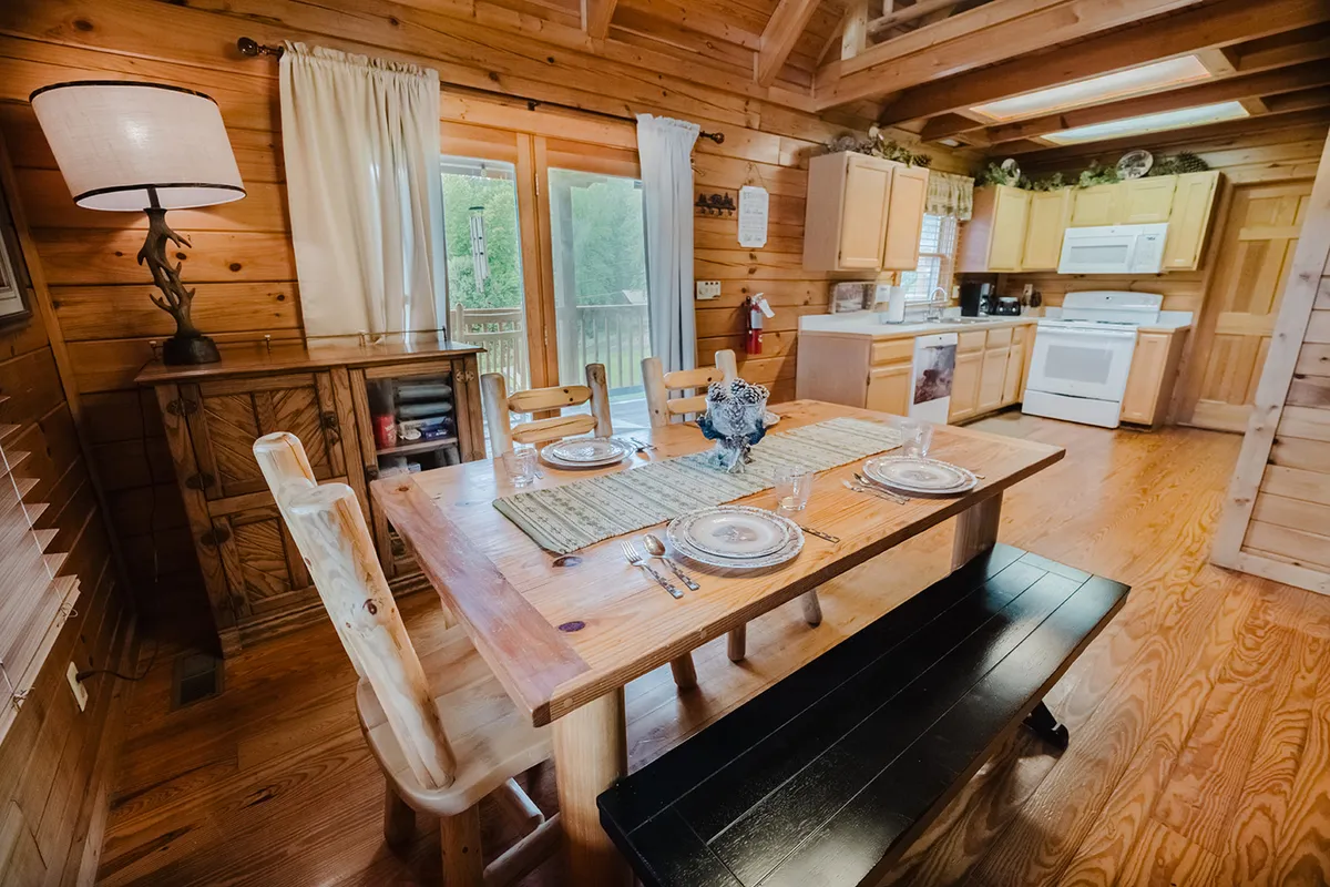 A cozy dining area featuring a wooden table, modern kitchen appliances, and large windows that frame serene outdoor views. The ambient lighting and decor create a space where friends can gather to cook, eat, and enjoy each other's company after a day of exploring.
