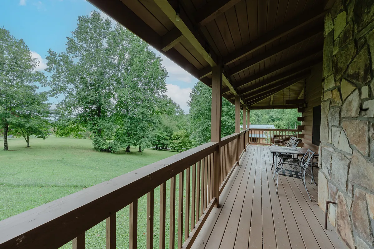 A spacious wooden deck bordered by verdant foliage, complete with comfortable seating. The setting conveys quiet moments for relaxation, intimate conversation, or simply soaking up the peace of nature, with an expansive view that encourages guests to savor both sunrise coffee and sunset toasts.