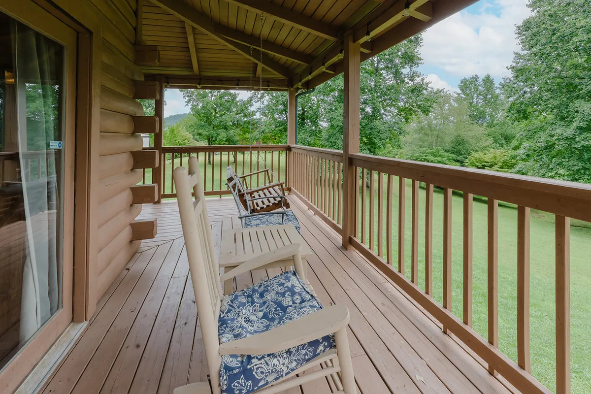 A serene cabin deck lined with wooden rocking chairs and a sturdy railing, set against a backdrop of vibrant greenery. The deck offers a tranquil spot to enjoy sunsets or take in the sounds of nature alongside your pet.