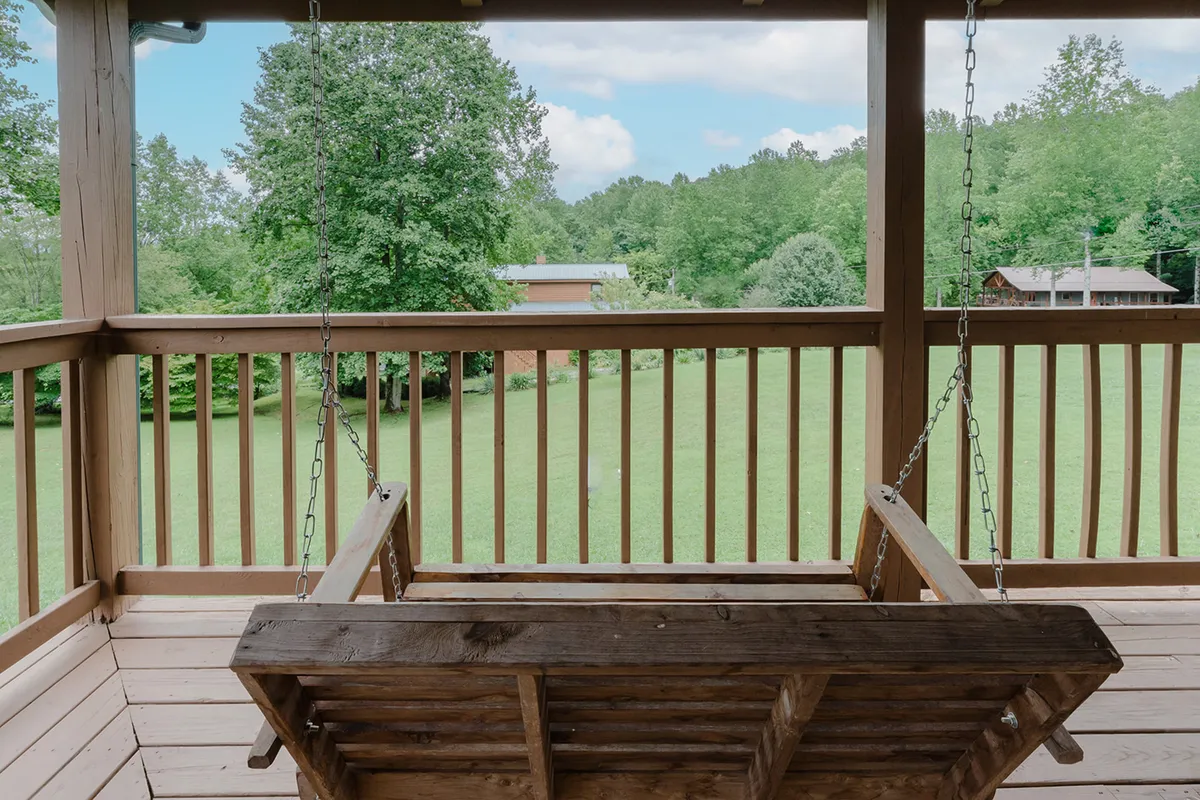 A peaceful scene featuring a swinging bench on a lush green lawn, framed by surrounding trees. The area is spacious, open, and ideal for enjoying the fresh mountain air or watching wildlife with your pet by your side.