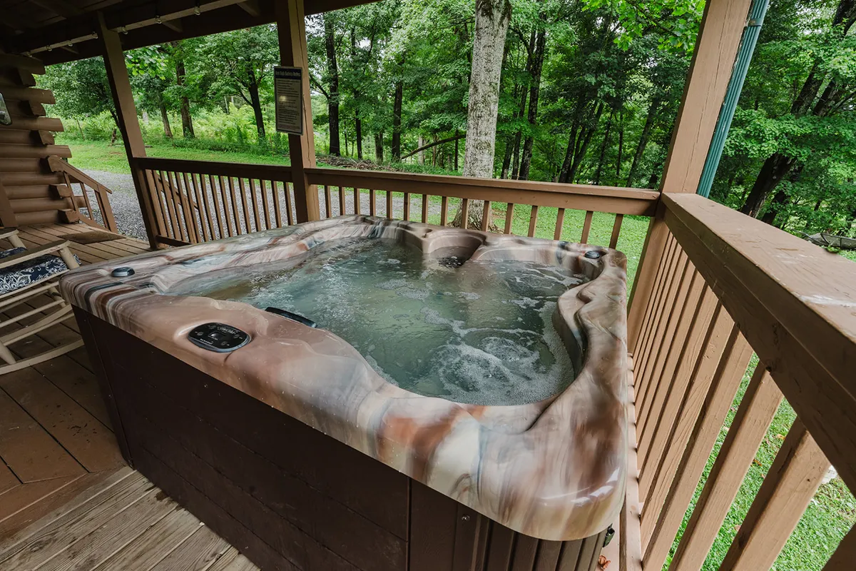 A tranquil exterior scene featuring a hot tub nestled on a wooden deck, surrounded by lush greenery. The view suggests relaxation and privacy, with the hot tub positioned for optimal stargazing and peaceful moments immersed in nature.