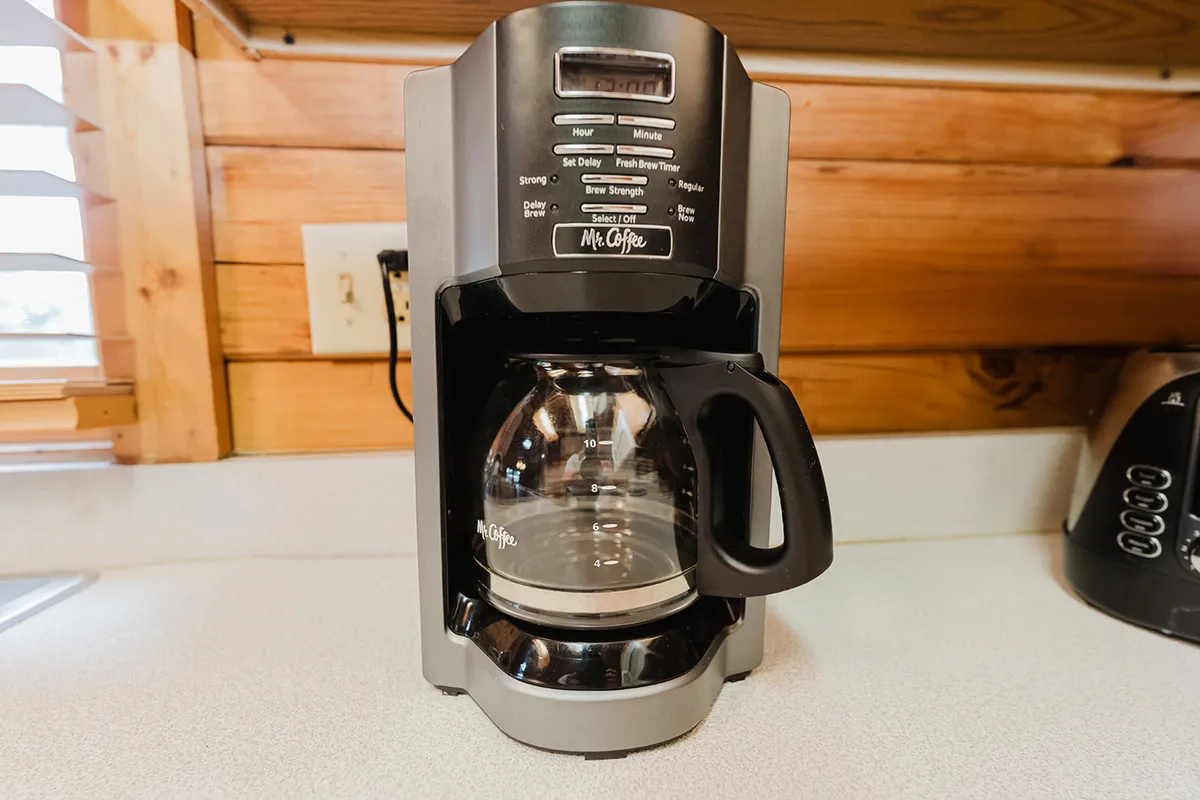 A close-up shot of a coffee maker and coffee pot on a cozy kitchen counter, evoking the morning ritual of brewing coffee. The scene hints at thoughtful extras and the warmth of sharing a morning beverage together.