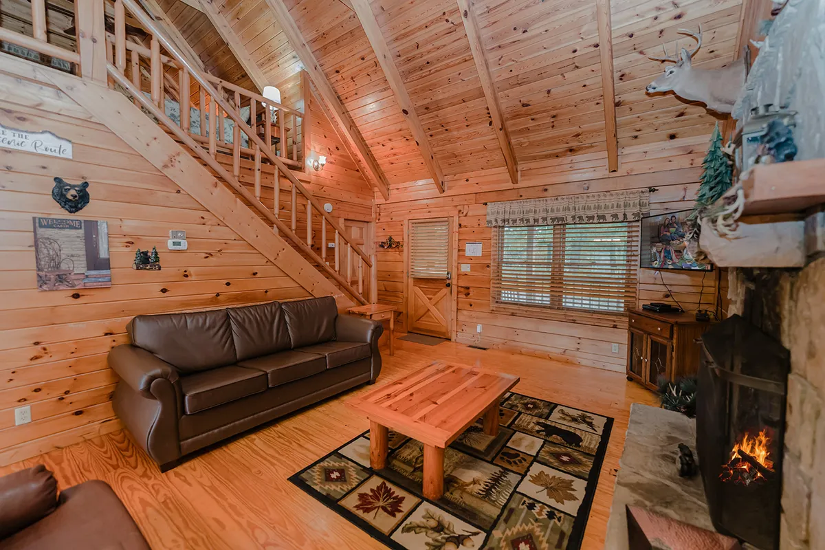 This image offers a broader view of the living room, showing a comfortable sofa, a coffee table perfect for board games or snacks, the fireplace, and a glimpse of a wooden staircase. Sunlight streams in, highlighting the welcoming atmosphere and the versatile space for family bonding or quiet relaxation.